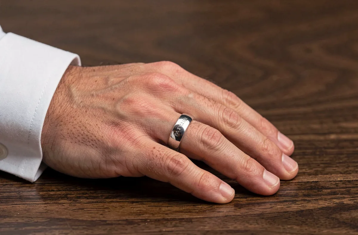 Bague homme en argent avec gravure intérieure visible, posée sur une surface en bois sombre, gros plan sur la main