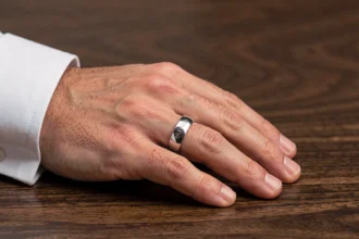 Bague homme en argent avec gravure intérieure visible, posée sur une surface en bois sombre, gros plan sur la main